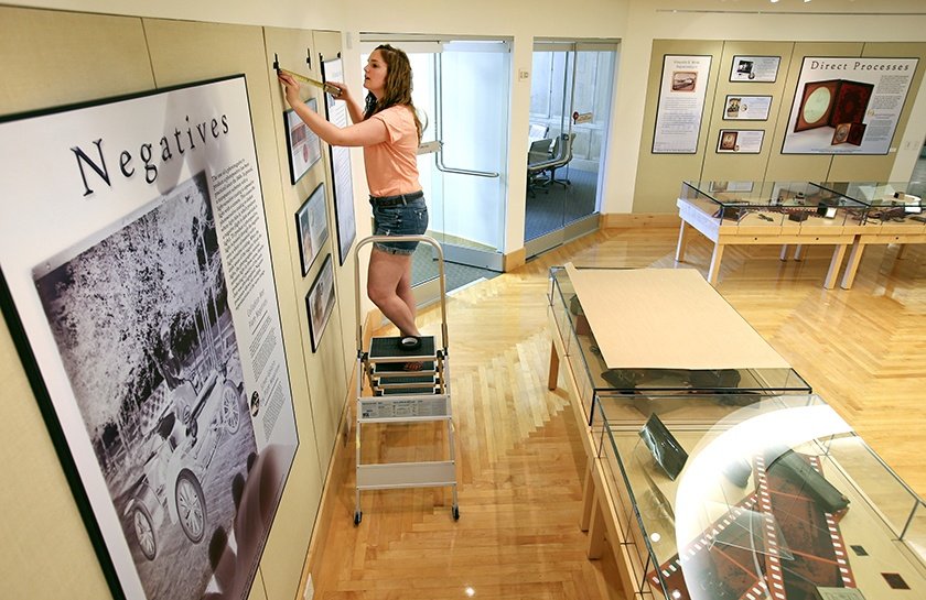 Student on a step ladder hanging exhibitions in the Clarke Historical Library's galleries