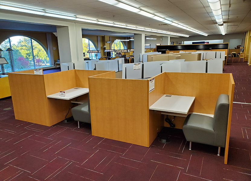 A large room in the library filled with individual library study pods, showing padded chairs, desk spaces and wooden dividers