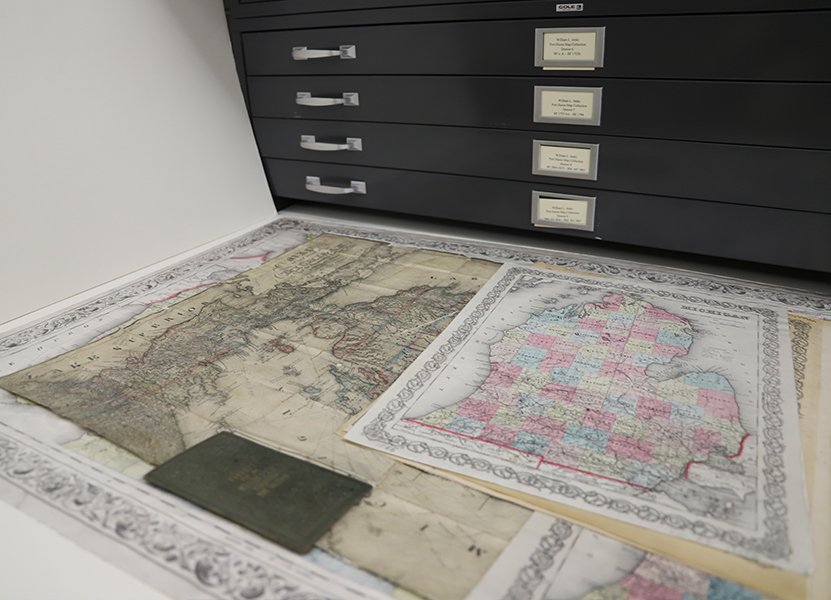 large flat maps depicting zones of Michigan from different times in history lying in a cabinet drawer