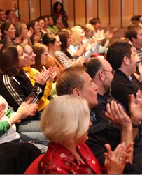 Crowd of people sitting in an auditorium smiling and applauding