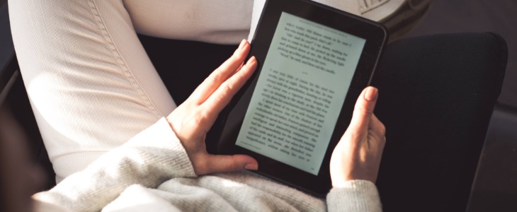 person wearing white jeans sitting causally reading ebook on tablet