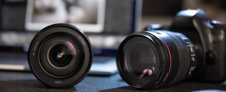 Tech Spotlight Imgs-1-Blog_Body Header_730x300 Image of a professional camera on the right and a camera lens on the left with a blurry laptop computer in the background.