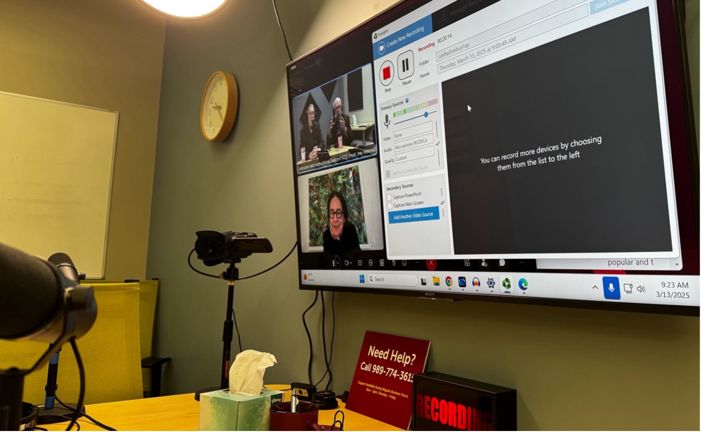 a screen on a wall showing a presentation and three video participants