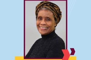 A picture of a woman in a black turtle neck sweater in front of a light blue background.