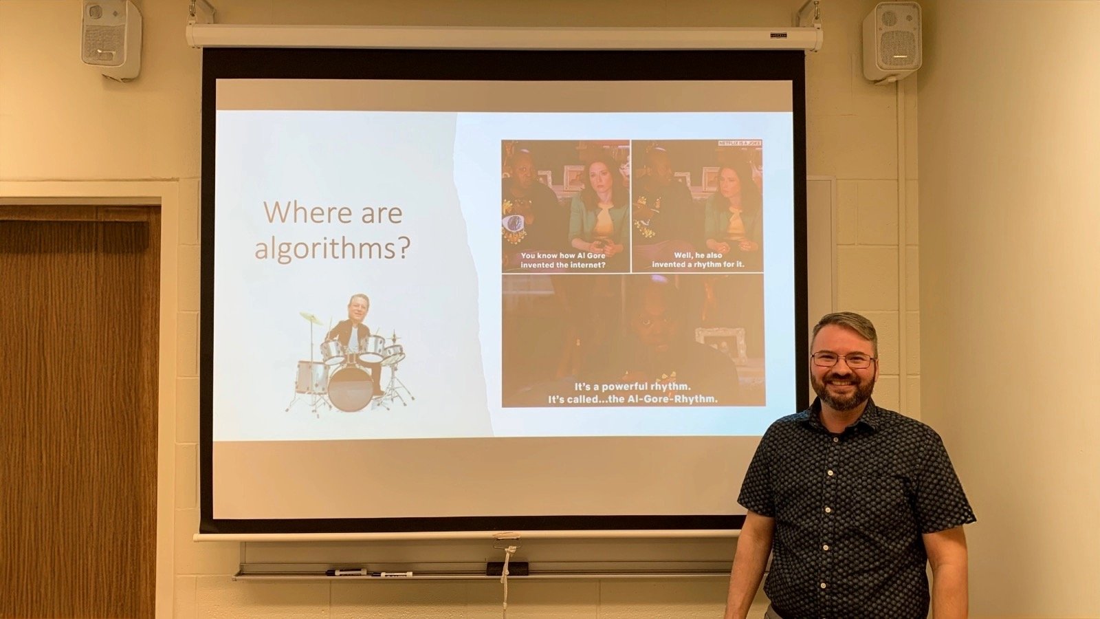 A man standing in front of a projector screen.