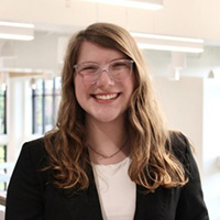 Britta_Williams_200x200 Britta Williams smiling in a professional headshot, wearing glasses and a black blazer in a bright indoor setting.