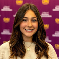 Carmella_Cortes_200x200 Carmella Cortes smiling in a professional headshot, wearing a light sweater with a maroon CMU logo backdrop.