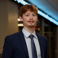 Cole_Carpenter_200x200 Cole Carpenter smiling in a professional headshot, wearing a suit and tie in an indoor setting.