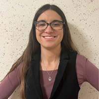 Jade_Walleman_200x200 Jade Walleman smiling in a professional headshot, wearing glasses and a black vest against a textured wall.