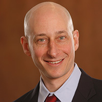 Spenser_Robinson_200x200 Spenser Robinson smiling in a professional headshot, wearing a suit and tie against a warm-toned background.