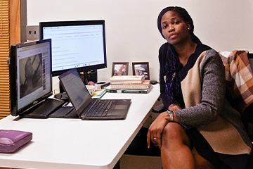 Professor Ekhomen Ehimen-Ebitibituwa sits at her desk in her office with multiple computer monitors, a laptop and books.