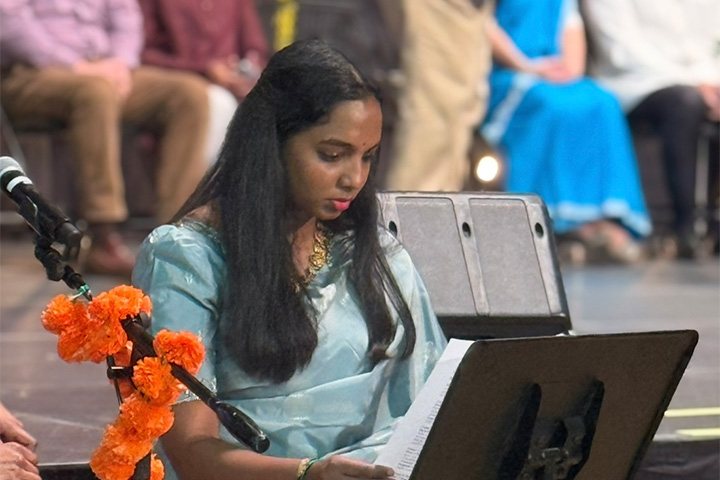 Vani Yerranagu arranges notes at a podium during the Diwali celebration. She is wearing a light blue sari and a gold necklace.