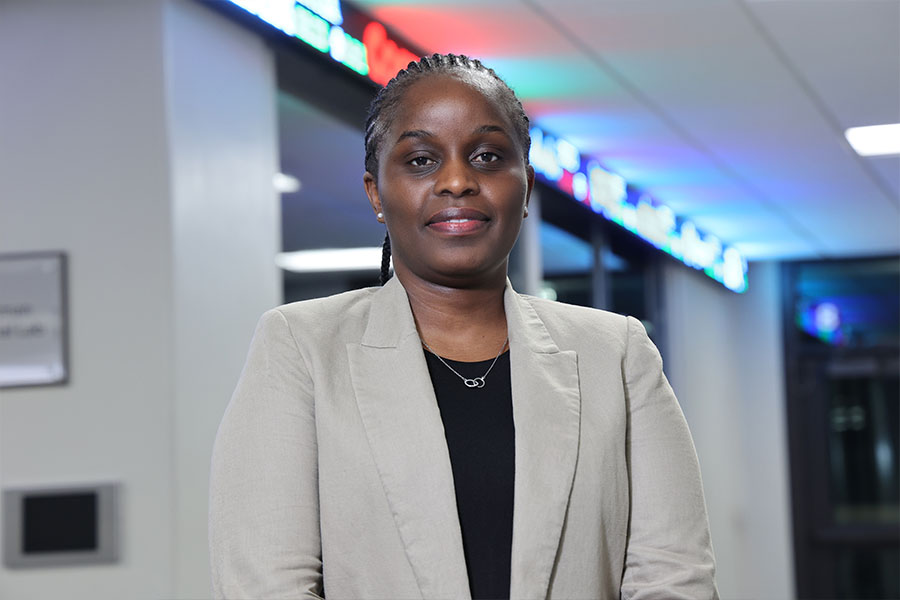 Judith Saungweme stands outside the Bloomberg Lab in Grawn Hall. The ticker display shines brightly behind her. She's wearing a tan blazer over a black shirt with a silver necklace. Her hair is braided into rows.