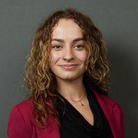 Savanna_Stewart_200x200 Savanna Stewart smiling in a professional headshot, wearing a maroon blazer against a dark background.