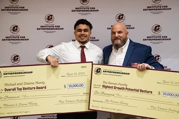 A student standing with a cmu faculty member holding up the student's two winning checks during the 2024 New Venture Challenge