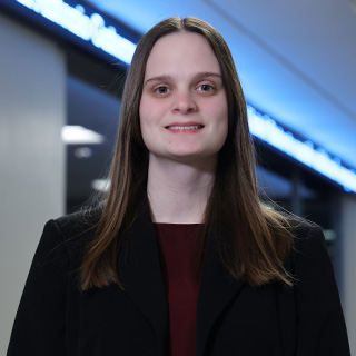 Kylea James stands outside the Bloomberg lab in Grawn Halls. She has long brown hair that is parted in the center and wears a black blazer with a maroon shirt.
