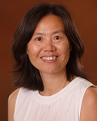 Lin Lan Xiao wears a white sleeveless shirt and smiles at the camera against an orange background. She is smiling and has shouldn't length black hair.