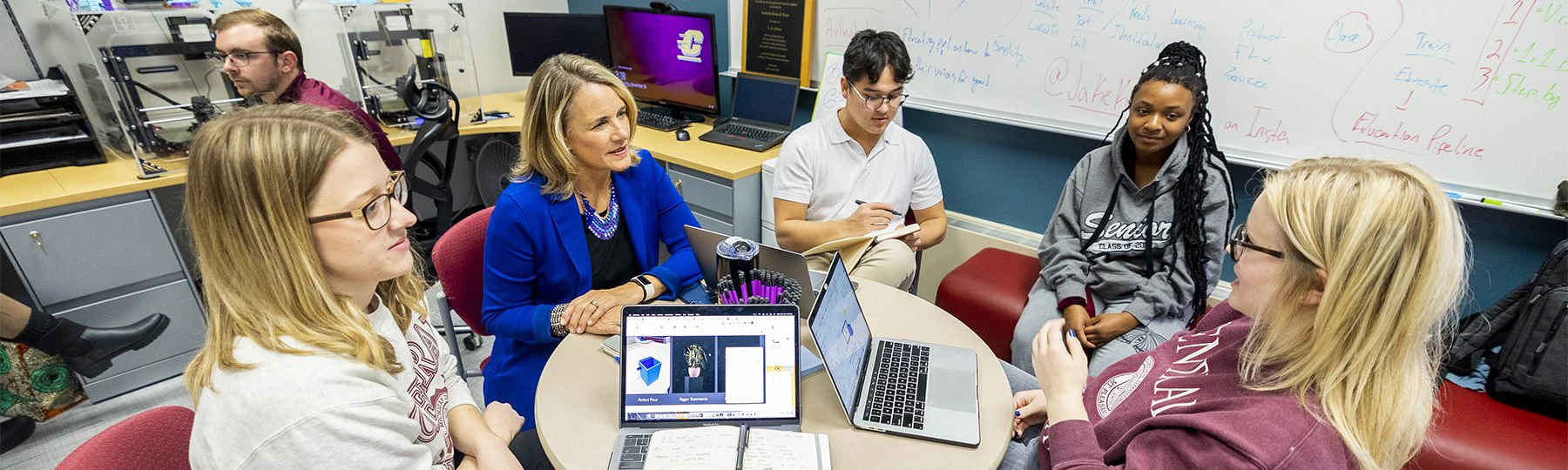 A group of students with a female professor having a discussion in the Entrepreneurship IDEA den.