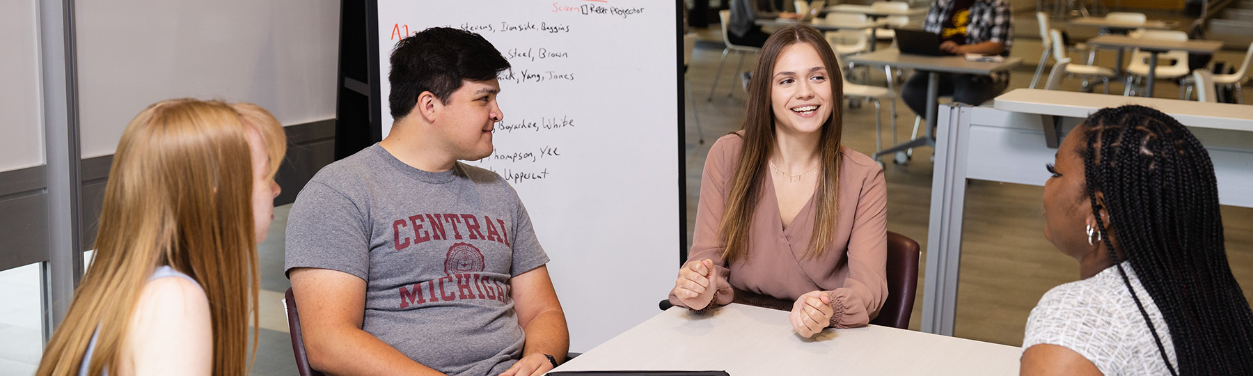Four Central Michigan University students sitting around a table, talking and working on a whiteboard.