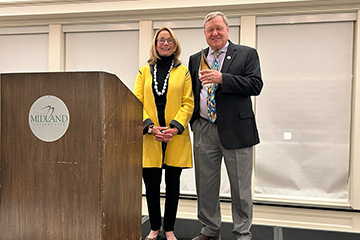 A man holding an amber award stands at a podium with a woman in a yellow cardigan.