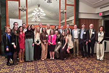 A group of medical students in business attire stand together smiling at the camera.