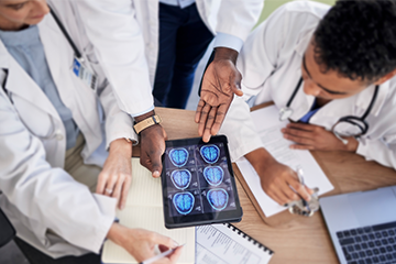 A group of doctors in white coats looking at a brain scan on a tablet.