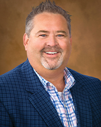 AaronSmith a man smiling in a blue plaid suit in front of a dark yellow background
