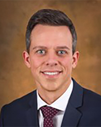 A man smiling in a blue suit and tie.