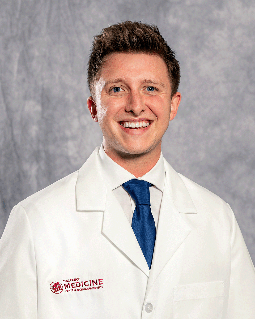A male CMU College of Medicine medical student wearing his white coat as he smiles for the camera.