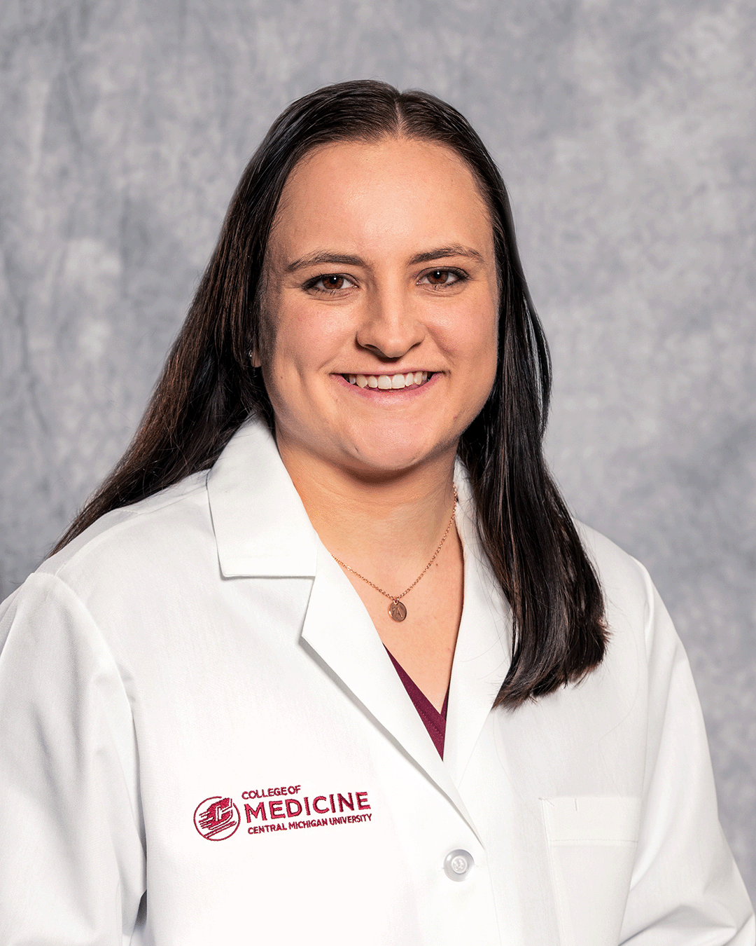 A female CMU College of Medicine medical student with long brown hair wearing her white coat as she smiles for the camera.