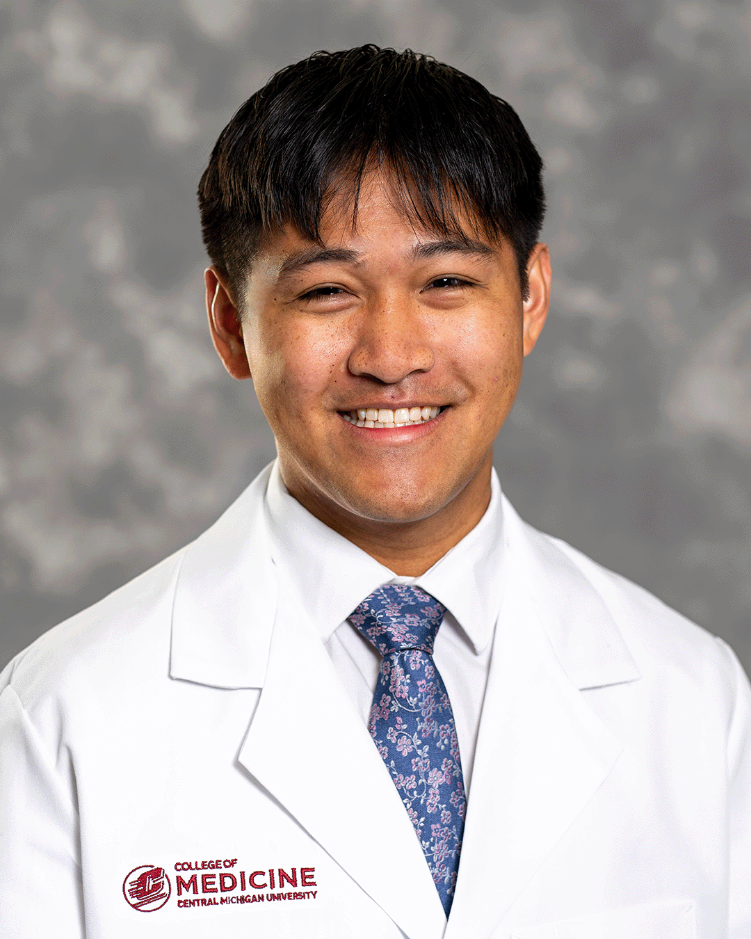 A male CMU College of Medicine medical student wearing his white coat as he smiles for the camera.