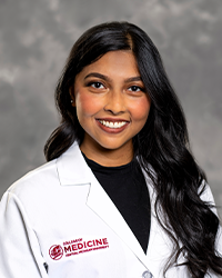 A female medical student in a white lab coat embroidered with a Central Michigan University College of Medicine logo.