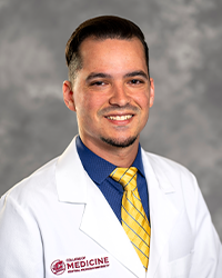 A male medical student in a white lab coat embroidered with a Central Michigan University College of Medicine logo.