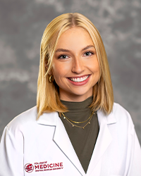 Krushena, Meghan 200 x 250 A female medical student in a white lab coat embroidered with a Central Michigan University College of Medicine logo.