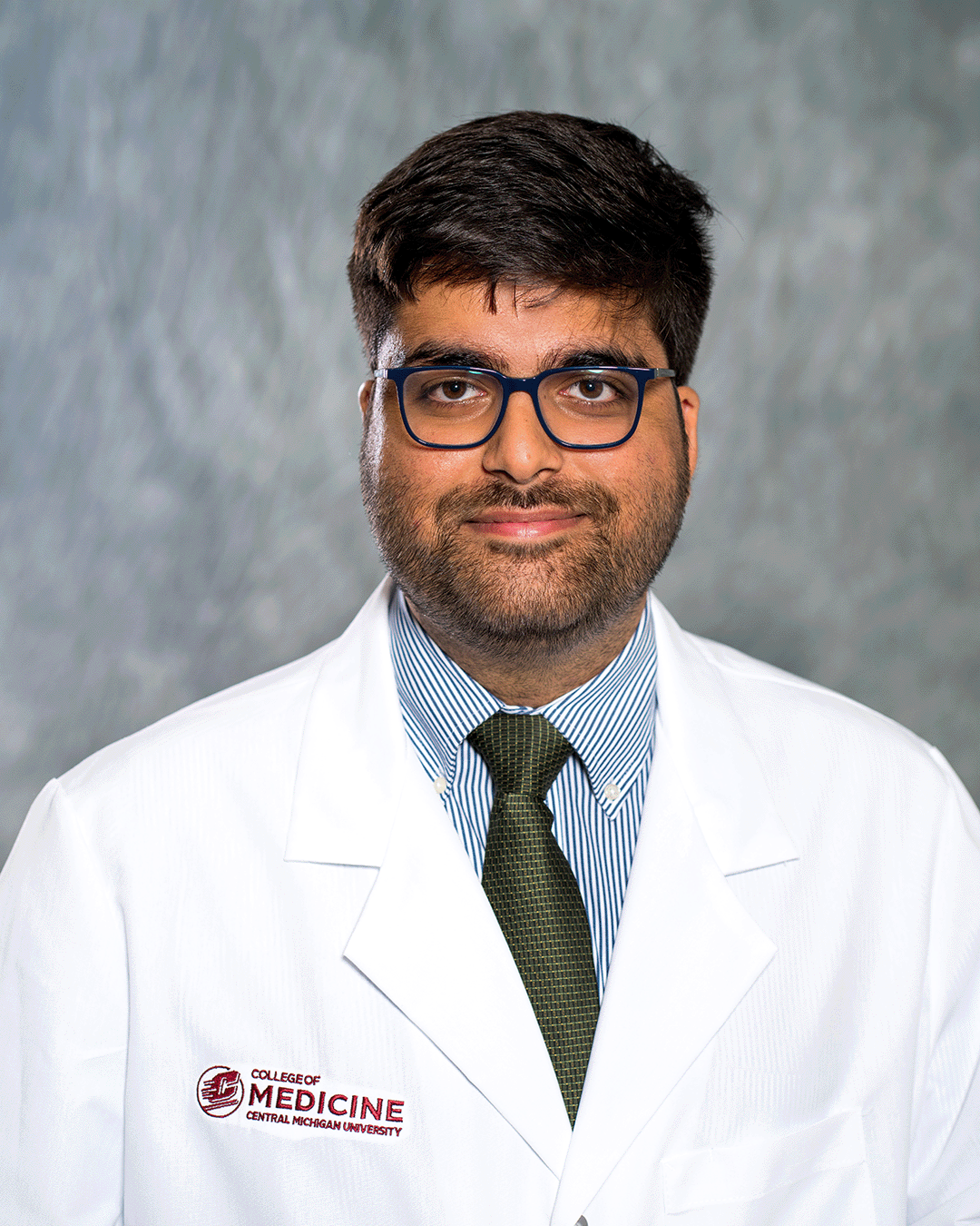 A male CMU College of Medicine medical student wearing her white coat as he smiles for the camera.