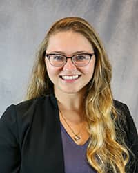 Headshot for Justin Czajka wearing a black blazer and blue top.