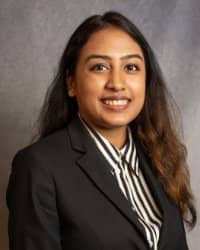 A women with long brown hair wearing a dark suit with a pin striped collared shirt smiling.