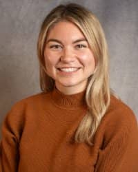 A women with long blonde hair wearing a rust colored sweater smiling.