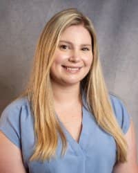 A woman with long blonde hair smiling in a light blue blouse.