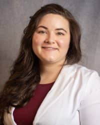 A woman with long dark hair wearing a white suit with a maroon shirt.