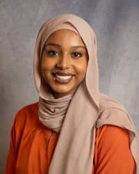 A women wearing a head scarf smiling in an orange shirt.