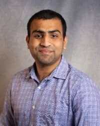 A man with dark hair wearing a blue plaid collared shirt.