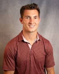 A man with short brown hair smiling in a red polo shirt.