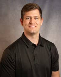 A man in a black shirt smiles for a professional headshot in front of a grey background.