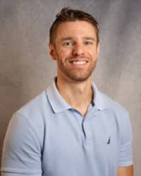 A man in a blue polo shirt smiles for a professional headshot against a grey background.