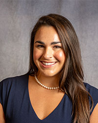 Joan Kronick is wearing a blue blouse with a pearl necklace.