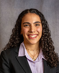 Jude Nowar has long curly hair and is wearing a black blazer and purple shirt.