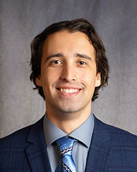 Alexander Szabo is wearing a blue blazer, grey shirt, and blue tie with designs.