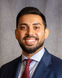 Danish Zamir in a blue suit with a red tie smiling