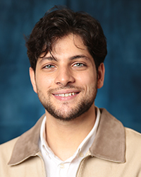 a man smiling for a picture, in a beige jacket